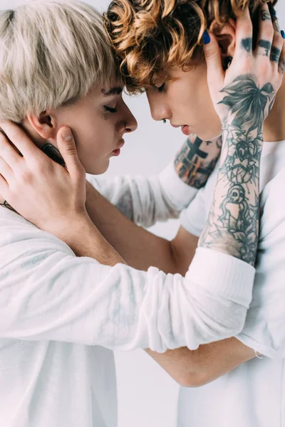 Novia con tatuajes abrazando novio con pelo rizado aislado en gris - foto de stock