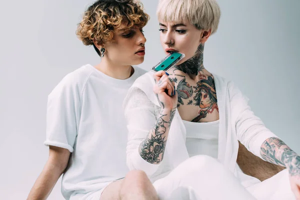 Attraktive blonde Frau hält Tonband in der Nähe des Mundes, während sie in der Nähe ihres Freundes sitzt, isoliert auf grau — Stockfoto