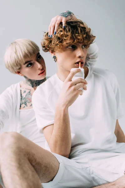 Man with curly hair holding cigarette in mouth near tattooed girl isolated on grey — Stock Photo