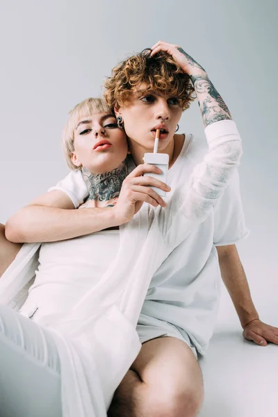 Homme avec les cheveux bouclés tenant cigarette dans la bouche près blonde tatoué fille isolé sur gris — Photo de stock