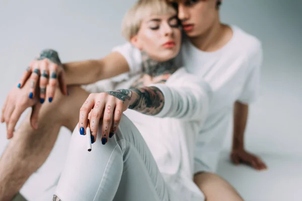 Foyer sélectif de cigarette dans la main de la femme assise avec l'homme isolé sur gris — Photo de stock