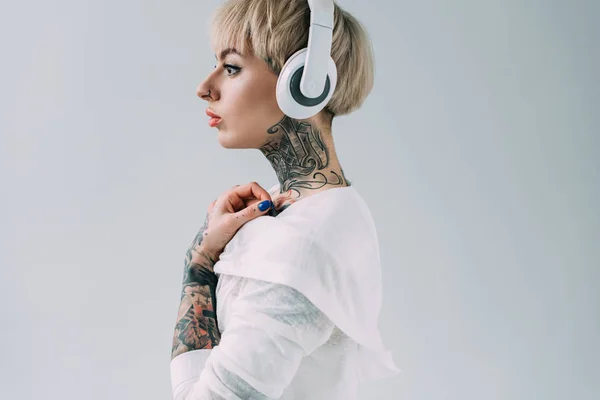 Vista lateral de mujer atractiva escuchando música en auriculares aislados en gris - foto de stock