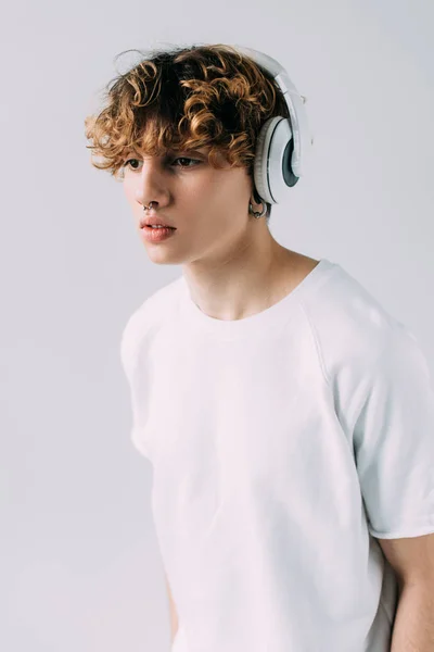 Hombre guapo escuchando música en auriculares aislados en gris - foto de stock