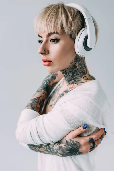 Atractiva mujer con tatuajes escuchando música en auriculares aislados en gris - foto de stock