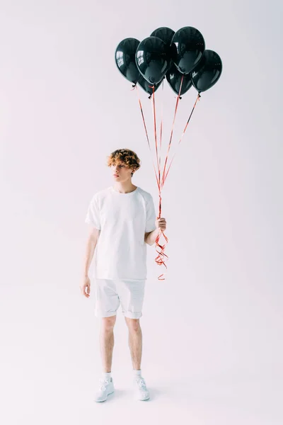 Handsome man with curly hair holding black balloons on grey background — Stock Photo