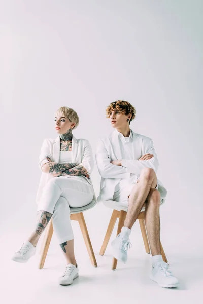 Homme et femme assis sur des chaises aux bras croisés sur fond gris — Photo de stock