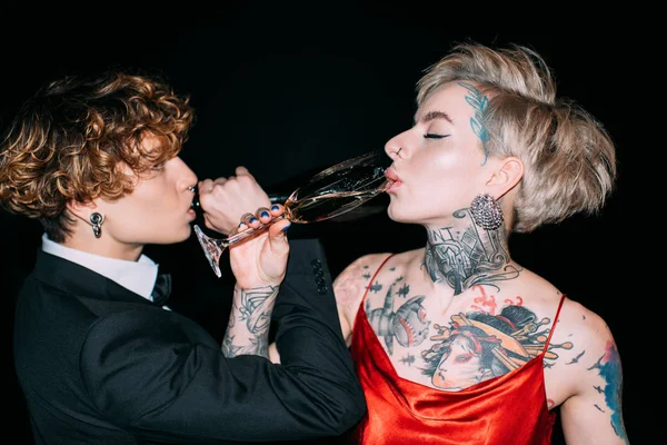 Жінка в червоній сукні і чоловік з кучерявим волоссям п'є шампанське ізольовано на чорному — стокове фото