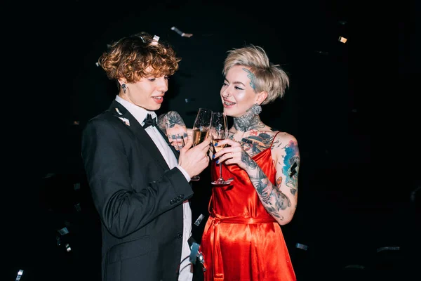 Cheerful man with curly hair toasting with glass of champagne with happy woman isolated on black — Stock Photo