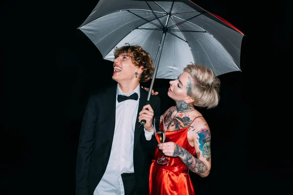 Alegre pareja de pie bajo paraguas y sonriendo aislado en negro - foto de stock