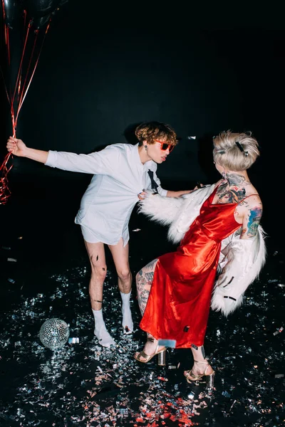 Ubriaco uomo guardando la donna in abito rosso, mentre tenendo palloncini sulla festa isolato su nero — Foto stock