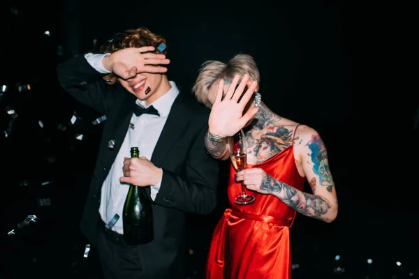 Couple covering face while holding alcohol drinks on party isolated on black — Stock Photo