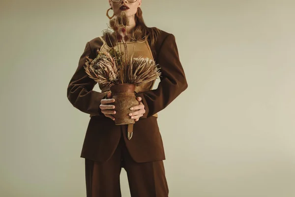 Vue recadrée d'une femme élégante tenant une cruche en argile avec des fleurs sèches isolées sur beige — Photo de stock