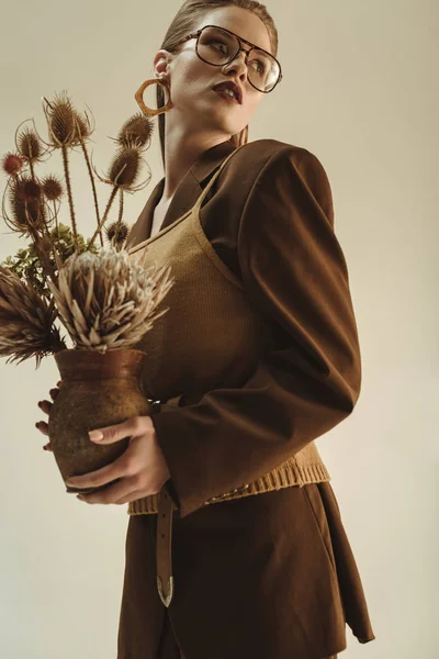 Attractive young woman holding clay jug with bouquet of dry flowers isolated on beige — Stock Photo
