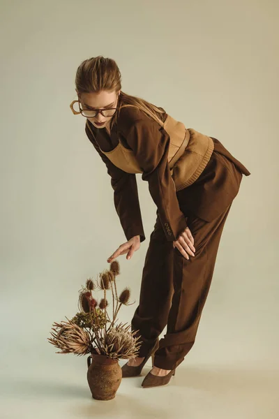 Donna alla moda che tiene la brocca di argilla con mazzo di fiori secchi su beige — Foto stock