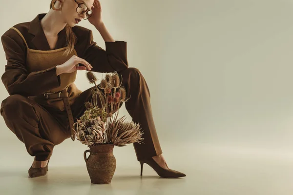 Atractiva mujer joven sosteniendo jarra de arcilla con ramo de flores secas en beige — Stock Photo