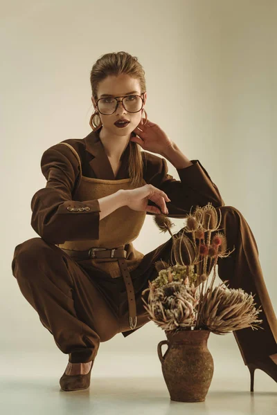 Bella donna alla moda che tiene la brocca di argilla con fiori secchi su beige — Foto stock