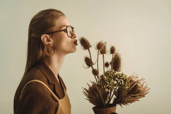 Attraente donna in stile vintage in possesso di brocca di argilla con mazzo di fiori secchi isolati su beige — Foto stock