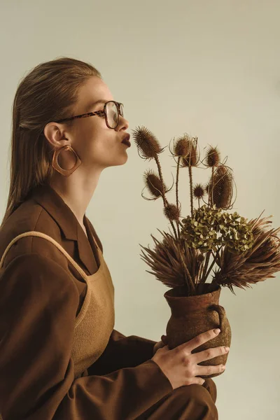 Belle femme de style rétro tenant cruche en argile avec bouquet de fleurs sèches isolées sur beige — Photo de stock