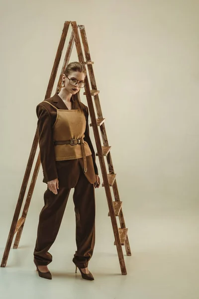 Привлекательная женщина в винтажном стиле позирует возле деревянной лестницы на бежевом — стоковое фото