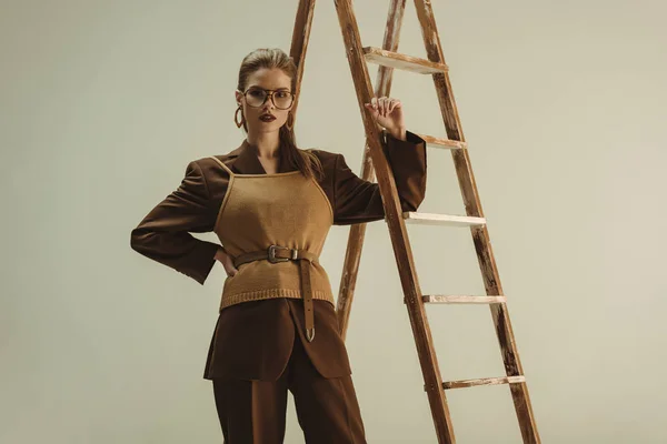 Beautiful fashionable model in retro style posing near wooden ladder isolated on beige — Stock Photo