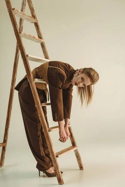 Jovem atraente em estilo vintage posando perto de escada de madeira no bege — Fotografia de Stock