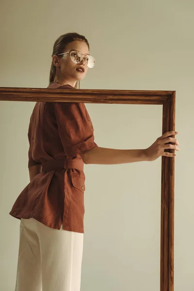 Красива модна дівчина позує з великою дерев'яною рамою ізольована на бежевому — стокове фото