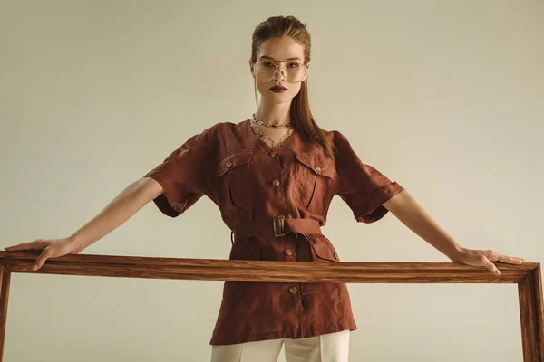 Attractive model posing with big wooden frame isolated on beige — Stock Photo