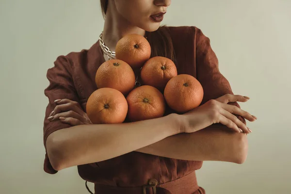 Vista cortada de menina elegante segurando laranjas frescas isoladas no bege — Fotografia de Stock