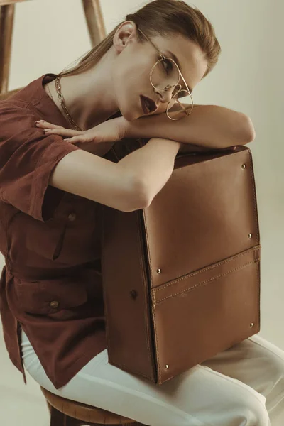Привлекательная модель с кожаной сумкой и сидя рядом с лестницей изолированы на бежевый — стоковое фото