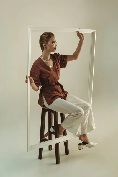 Atractiva mujer posando en taburete con marco blanco grande - foto de stock