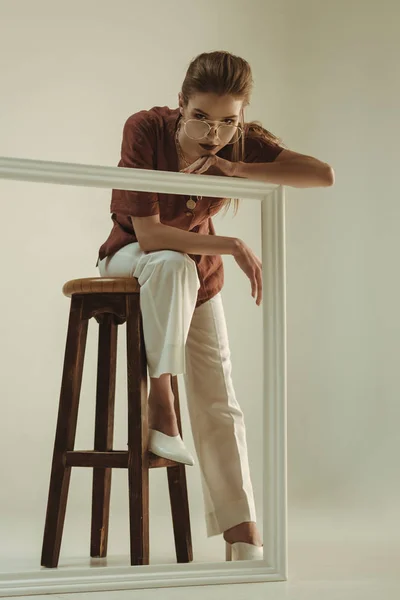 Привлекательная модная женщина позирует на стуле с большой белой рамкой — стоковое фото