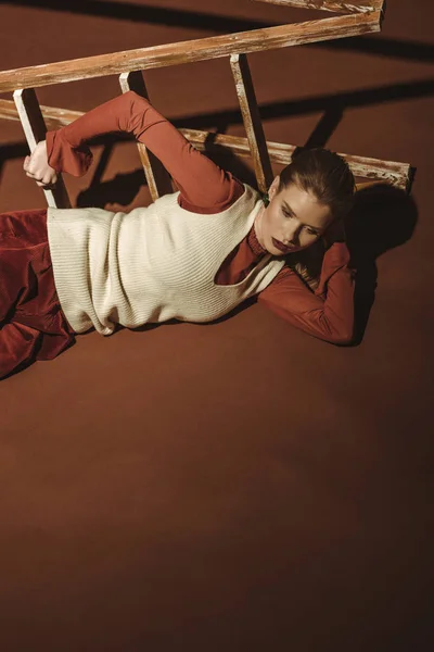 Mujer joven de moda en estilo retro posando cerca de escalera de madera en marrón - foto de stock