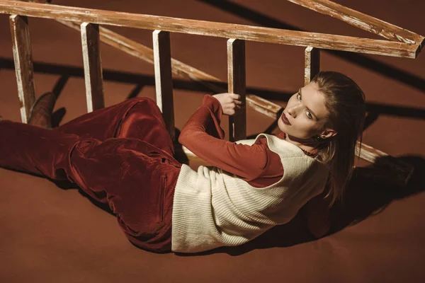 Привлекательная женщина в модном стиле позирует возле деревянной лестницы на коричневом — стоковое фото
