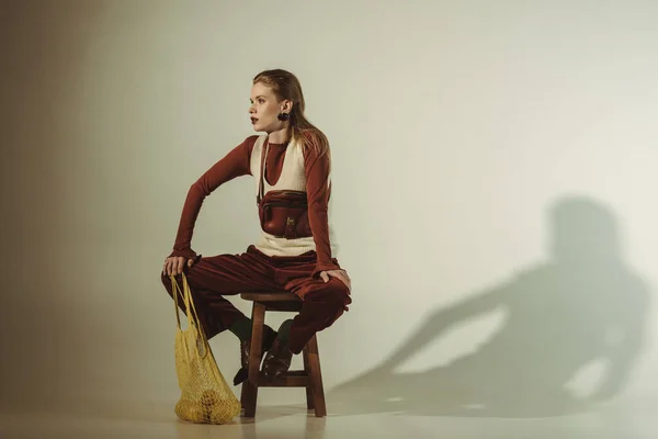 Привлекательная модель сидит на стуле с лимонами в струнном мешке на бежевом — стоковое фото
