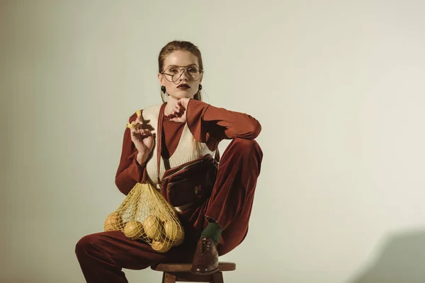 Belle femme à la mode assise sur un tabouret avec des citrons dans un sac à ficelle — Photo de stock