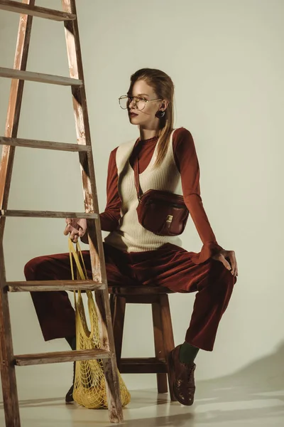 Stylische junge Frau mit Zitronen in String Bag posiert nahe Leiter — Stockfoto