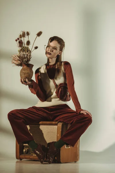 Attraktive Frau hält einen Strauß trockener Blumen in der Hand und sitzt auf einem Vintage-Fernseher in Beige — Stockfoto