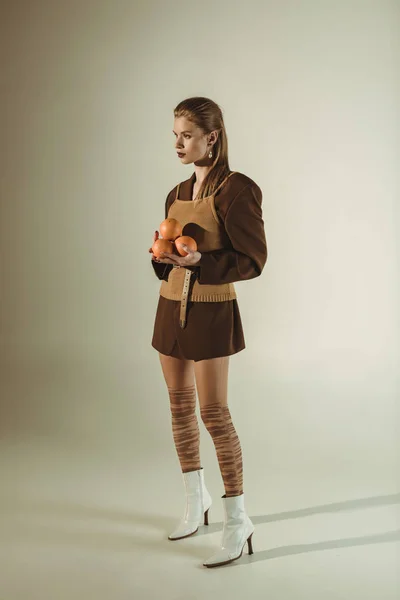 Beautiful fashionable girl in retro style holding fresh oranges on beige — Stock Photo