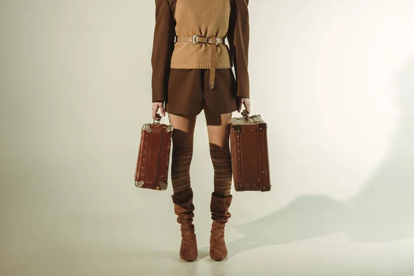 Cropped view of young woman holding vintage travel bags on beige — Stock Photo
