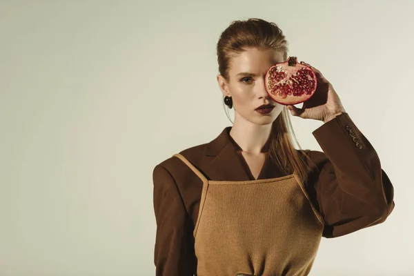 Beautiful young woman holding half of pomegranate in front of the face isolated on beige — Stock Photo