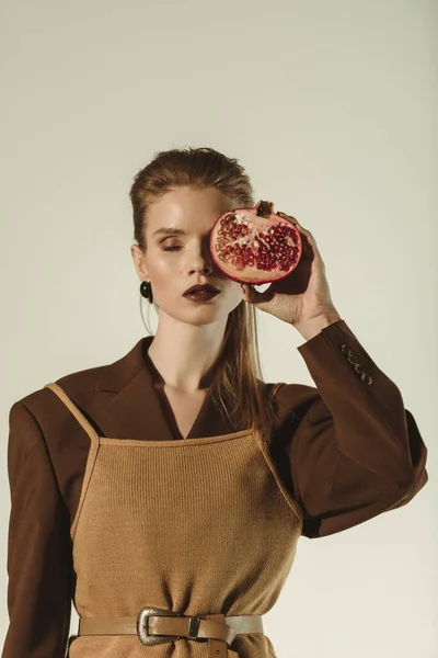 Attractive woman with closed eyes holding half of pomegranate in front of the face isolated on beige — Stock Photo