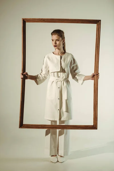 Schöne modische Frau im weißen Outfit posiert mit großem Holzrahmen — Stockfoto