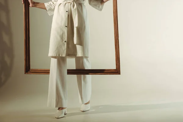 Cropped view of woman in white trendy outfit posing with big wooden frame — Stock Photo