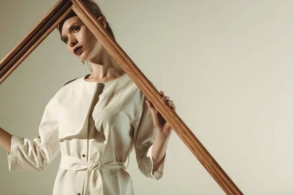 Attraente giovane donna in abito bianco alla moda in posa con grande telaio in legno isolato su beige — Foto stock