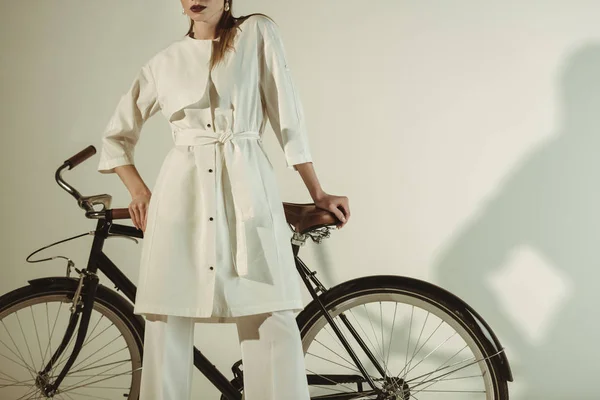 Vue recadrée de fille à la mode en tenue blanche posant sur le vélo — Photo de stock
