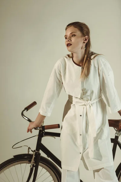 Chica de moda en traje blanco posando en bicicleta aislado en beige - foto de stock