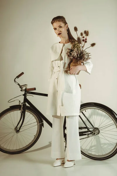 Fille à la mode posant avec bouquet de fleurs sèches près de beige — Photo de stock