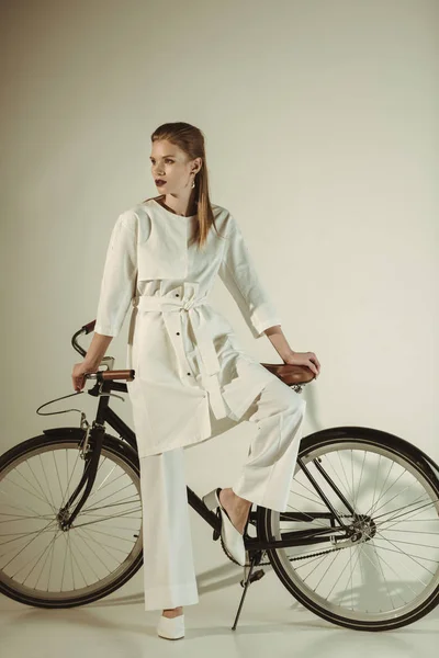 Atractiva chica con estilo en traje blanco posando en bicicleta - foto de stock