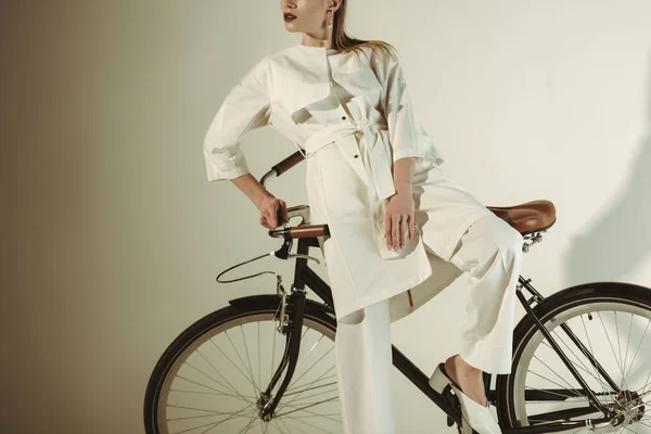 Vue recadrée de fille élégante en tenue blanche posant sur le vélo — Photo de stock