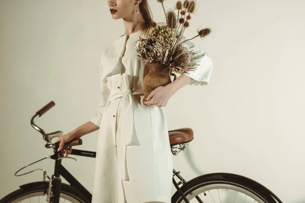 Vue recadrée de femme élégante posant avec bouquet de fleurs sèches près du vélo — Photo de stock